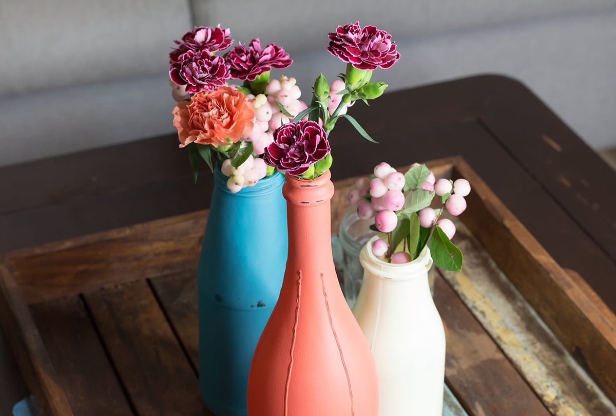 Mit Kreidefarbe bemalte Vasen aus alten Glasflaschen im Landhaus-Stil auf Holztisch